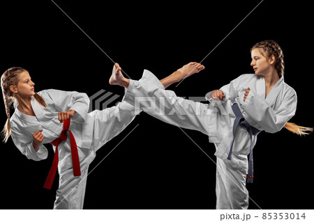 Two young girls, teens, taekwondo athletes training together isolated over dark background. Concept of sport, education, skills Two young girls, teens, taekwondo athletes training together isolated over dark background. Concept of sport, education, skills 85353014