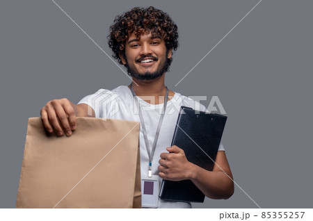 Pleased deliveryman posing for the camera against the gray background Pleased deliveryman posing for the camera against the gray background 85355257
