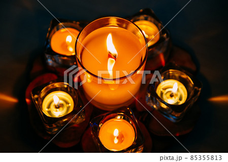 Large wax candle in glass candlestick burns among small flat candles. View from above. Relaxation 85355813