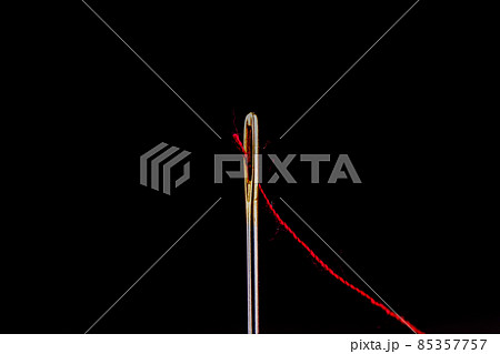 Red thread in the eye of a needle isolated on a black background. Red thread in the eye of a needle isolated on a black background. 85357757