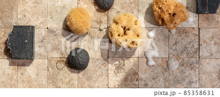 Bamboo charcoal bathroom accessories - konjac bamboo charcoal black sponge, handmade black soap and natural sea sponges with soap foam on earth toned stone tales top view 85358631
