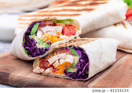 Grilled chicken wraps with red cabbage, avocado, tomato, lettuce and cheddar cheese, on wooden board Grilled chicken wraps with red cabbage, avocado, tomato, lettuce and cheddar cheese, on wooden board 85359154