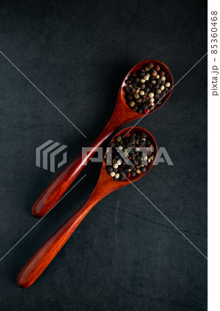 Wooden spoon with mix of pepper on a black background. Dried aromatic spice. 85360468