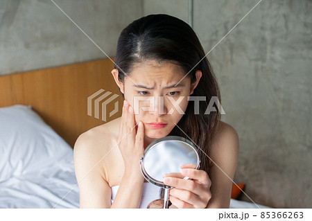 Portrait of Asian woman worry about her face when she saw the problem of acne and scar by the mini mirror. Conceptual shot of Acne & Problem Skin on female face. Portrait of Asian woman worry about her face when she saw the problem of acne and scar by the mini mirror. Conceptual shot of Acne & Problem Skin on female face. 85366263
