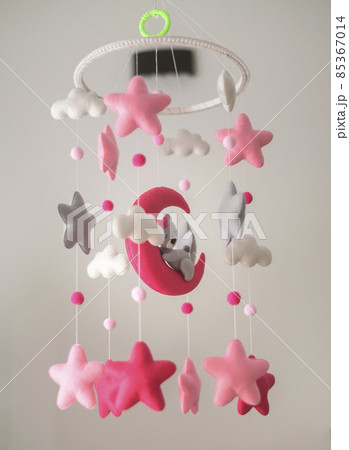 Baby crib hangings, Felt cot mobile with soft plushie stars clouds and moon with sleeping teddy, Cot isolated against a neutral color background. Beautiful music toy over the crib in the baby room. 85367014