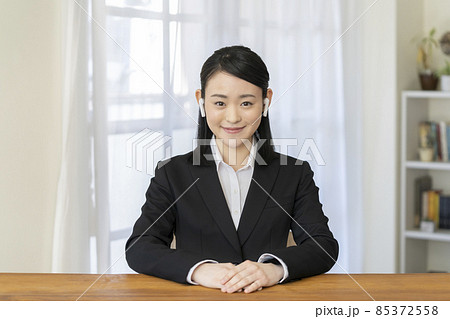 ワイヤレスイヤホンをつけたカメラ目線で笑顔のスーツ姿の若い女性 ワイヤレスイヤホンをつけたカメラ目線で笑顔のスーツ姿の若い女性 85372558
