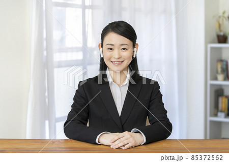 ワイヤレスイヤホンをつけてカメラ目線で話す笑顔のスーツ姿の若い女性 85372562