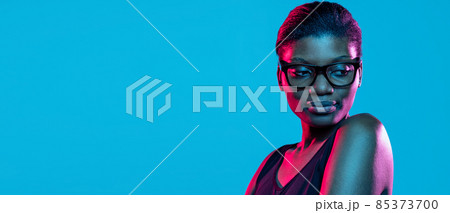 Flyer with young beautiful dark skinned woman posing isolated on blue studio background in neon light. Flyer with young beautiful dark skinned woman posing isolated on blue studio background in neon light. 85373700