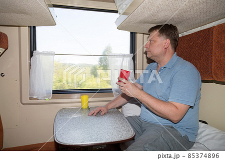 A full grown man in a train compartment is sitting at a table with a mug of tea, the concept of lunch on a journey 85374896