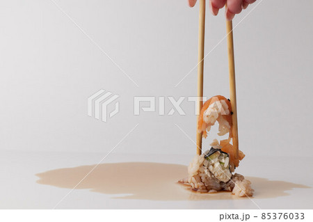 a hand and Chinese chopsticks holds a roll over other sushi, a portion of Asian food, rolls 85376033