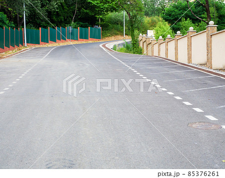 Freshly laid asphalt on the road with markings and fences along and green trees Freshly laid asphalt on the road with markings and fences along and green trees 85376261