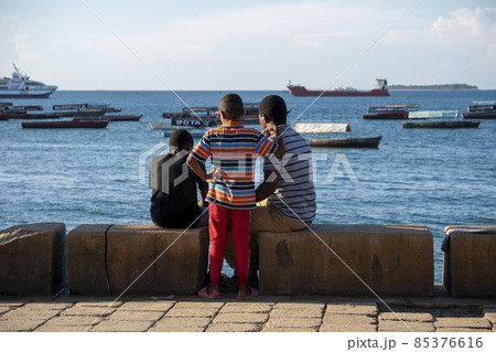 Black African Guys are sit on the Embarkment and Look in the Sea with boats in Stone Town, Zanzibar, Tanzania 85376616