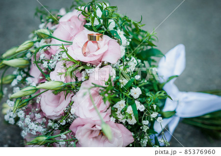 Pink with green flower bouquet and pair of golden rings lies on the asphalt Pink with green flower bouquet and pair of golden rings lies on the asphalt 85376960