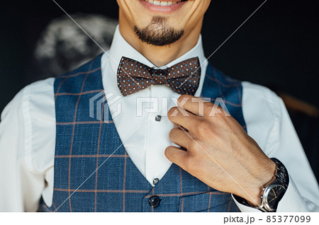 Handsome bearded man straightens a bow tie around his neck. Stylish men's accessory 85377099