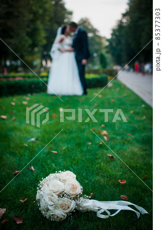 Flower bouquet lying on the grass and couple of people on the background Flower bouquet lying on the grass and couple of people on the background 85377303