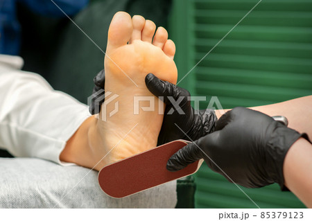 Peeling of Heels. Hands of pedicure master scrape dead from heel skin by special grater in spa salon. 85379123