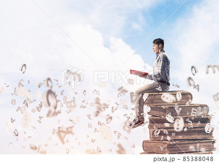 Man student on stack reading book and symbols flying around 85388048
