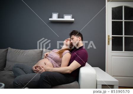 Pregnant husband and wife sitting cuddled up on the sofa contemplating their offspring. A woman with an advanced pregnancy. Pregnant husband and wife sitting cuddled up on the sofa contemplating their offspring. A woman with an advanced pregnancy. 85390570