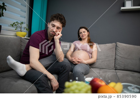 A married couple sits on the sofa at their home and the husband worries about what it will be like after the birth. Pregnant woman. A married couple sits on the sofa at their home and the husband worries about what it will be like after the birth. Pregnant woman. 85390590