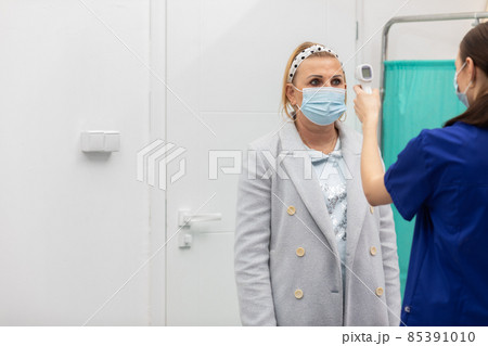 A nurse stands at the entrance of the clinic and checks the temperature of incoming patients to eliminate those infected with COVID-19 A nurse stands at the entrance of the clinic and checks the temperature of incoming patients to eliminate those infected with COVID-19 85391010