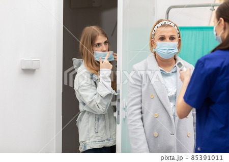 A nurse stands at the entrance of the clinic and checks the temperature of incoming patients to eliminate those infected with COVID-19 85391011