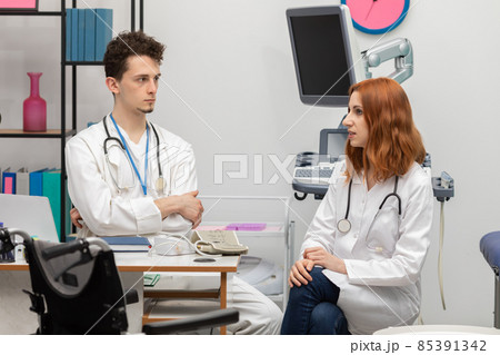 A young doctor talks to a redheaded intern about his next patient. GP. Doctor's office A young doctor talks to a redheaded intern about his next patient. GP. Doctor's office 85391342