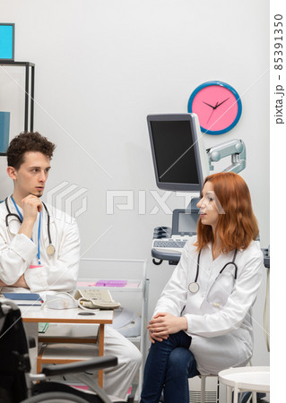 A young doctor talks to a redheaded intern about his next patient. GP. Doctor's office A young doctor talks to a redheaded intern about his next patient. GP. Doctor's office 85391350