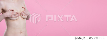 Young nude woman gently covers her breasts with both hands. Portrait on pink background. Close-up view. Panoramic frame. Young nude woman gently covers her breasts with both hands. Portrait on pink background. Close-up view. Panoramic frame. 85391689