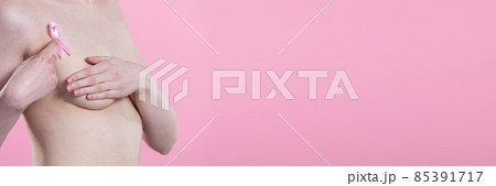 Undressed woman holds pink ribbon over breast pressing index finger against body. Panoramic frame. 85391717