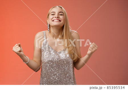 Sweet taste win. Charming happy blond girl rejoicing triumphing raise head up close eyes smiling broadly clench fists victory celebration gesture achieve dream come true, standing red background 85395534
