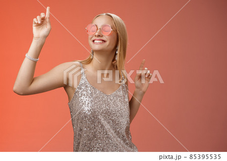Delighted carefree attractive stylish millennial blond woman celebrating partying having fun wear sunglasses trendy silver dress dancing closed eyes broad smile waving hands up, red background Delighted carefree attractive stylish millennial blond woman celebrating partying having fun wear sunglasses trendy silver dress dancing closed eyes broad smile waving hands up, red background 85395535