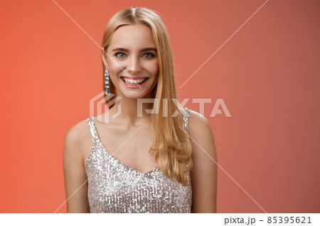 Charming glamour fabulous adult 25s blond woman in elegant silver dress shiny earrings smiling happily take part interesting conversation talking look friendly grinning, standing red background Charming glamour fabulous adult 25s blond woman in elegant silver dress shiny earrings smiling happily take part interesting conversation talking look friendly grinning, standing red background 85395621