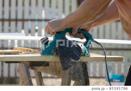 a worker processes a board with an electric plane a worker processes a board with an electric plane 85395796