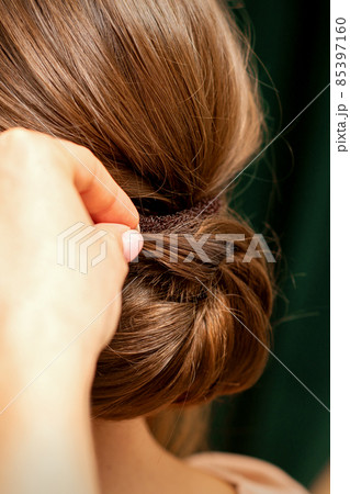 Hands of hairdresser making french twist hairstyle of an unrecognizable young brunette woman in a beauty salon, back view, close up. 85397160