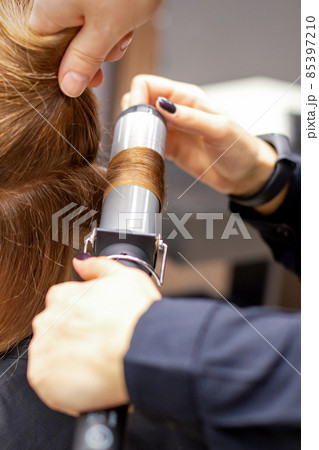 Hands of female hairstylist curls hair client with a curling iron in a hairdressing salon, close up. Hands of female hairstylist curls hair client with a curling iron in a hairdressing salon, close up. 85397210