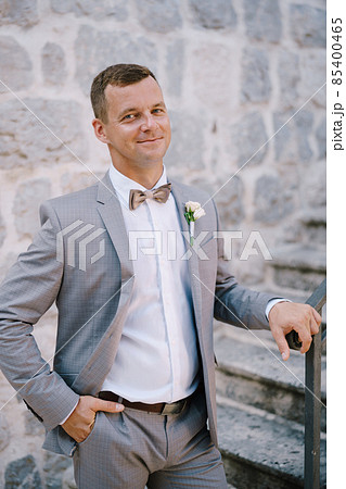Groom stands on a stone staircase with his hand on the handrail Groom stands on a stone staircase with his hand on the handrail 85400465