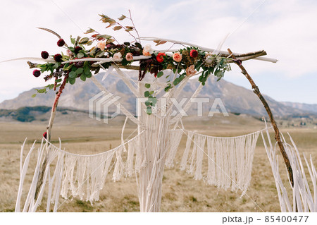 Wedding arch decorated with macrame, flowers and branches stands in the field 85400477
