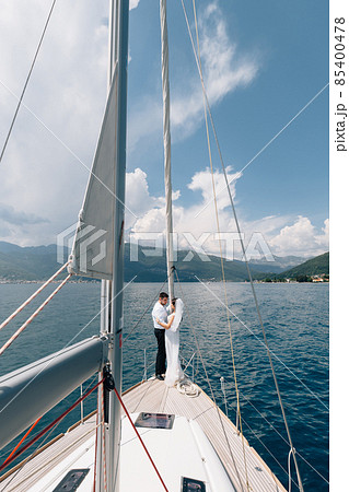 The bride and groom are hugging while standing on the bow of a white yacht sailing in the Bay of Kotor  85400478