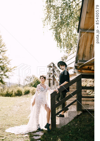 Groom and bride stand on the stone steps near the wooden hut Groom and bride stand on the stone steps near the wooden hut 85400579