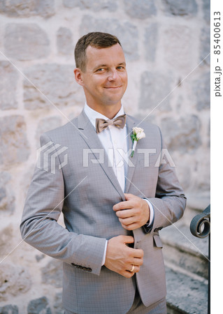Groom holds the lapels of his jacket with his hands and stands on the stone stairs Groom holds the lapels of his jacket with his hands and stands on the stone stairs 85400613