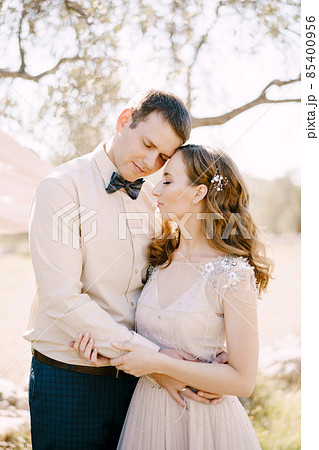 Groom hugs bride while standing under the tree. Portrait 85400956