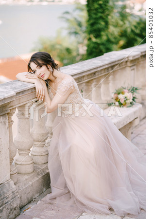 Bride sits on a stone bench with her head resting on a stone balustrade Bride sits on a stone bench with her head resting on a stone balustrade 85401032
