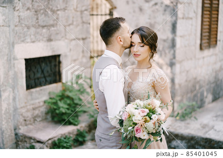Groom kisses bride forehead near the stone building. Portrait Groom kisses bride forehead near the stone building. Portrait 85401045