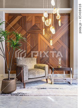 Modern beige armchair, small coffee table, planter, and modern tall glass chandelier, and decorated wood cladding wall 85408416