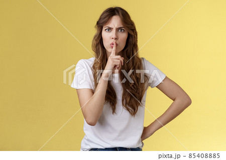 Shut your mouth no talking during concert. Serious-looking strict displeased adult sister demand sit silent hushing hold index finger pressed lips frowning angry shushing yellow background 85408885