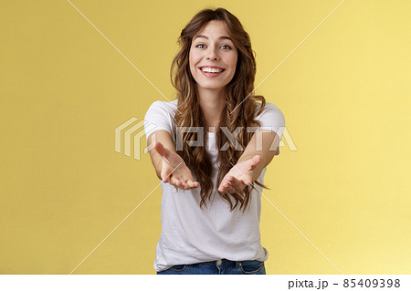 Let me hold it. Sincere tender touched charming curly-haired girl reaching you extend arms smiling lovely tempting grab precious thing receive gift stand yellow background grateful cheerful 85409398