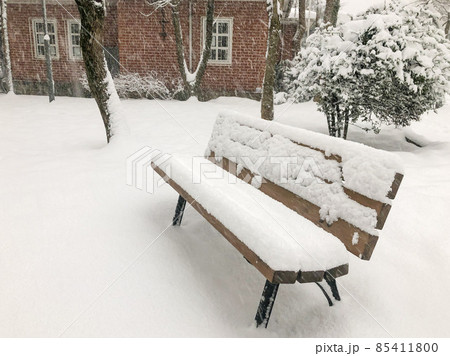 empty bench under snow in winter at garden of a house while snowing 85411800
