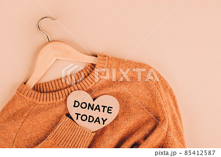 Clothing donations, conscious and environmentally friendly consupmtion - new trends in shopping. Christmas donations concept. Sweaters on beige background with copy space. Quote - donate today 85412587