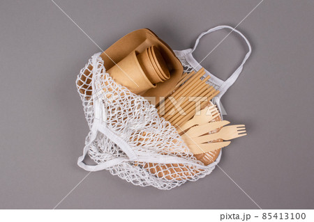 Eco-friendly tableware - kraft paper food cups, plates and containers with wooden cutlery in cotton bag on gray background with copy space. Street food paper packaging 85413100