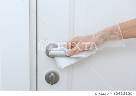 Cleaning door handles with wet wipe and white gloves. Sanitize surfaces prevention in hospital and public spaces against corona virus. Woman hand using towel for cleaning home room door link. 85413150